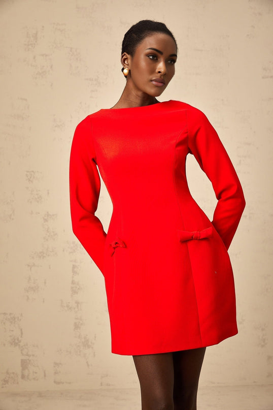 A red mini dress with long sleeves and a bowknot detail worn by a model against a plain background