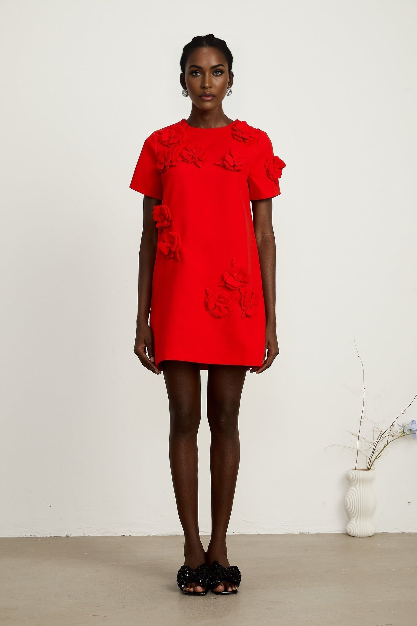 A red mini dress with short sleeves and floral details worn by a model against a plain background