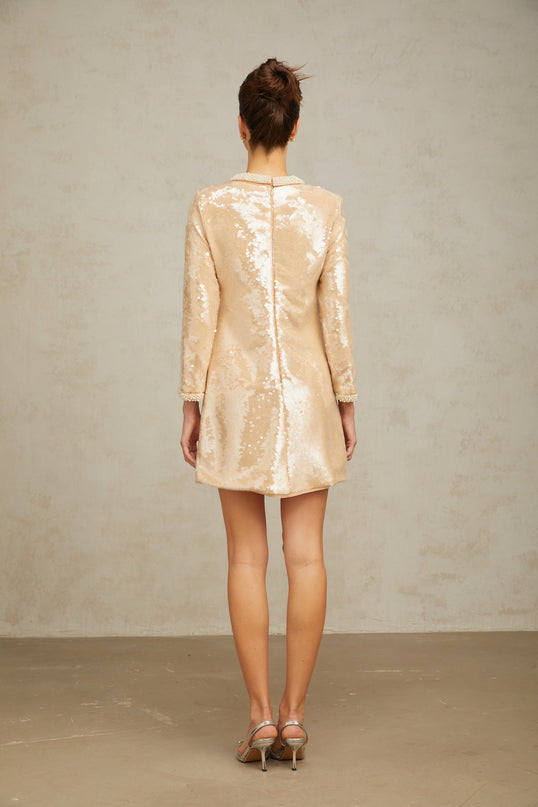 A short beige mini dress adorned with faux pearls and sequins creating a shimmering neutral toned look