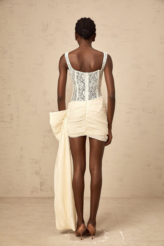 A short beige mini dress with floral lace details and a bow accent featuring a pencil skirt silhouette