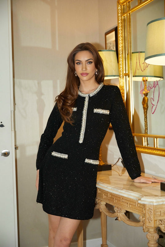 A short black knit mini dress adorned with crystal sequins featuring a formfitting silhouette and sparkling embellishments throughout