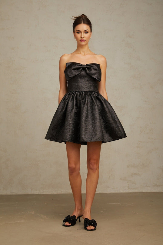 A short black metallic mini dress with a prominent bow detail on the front