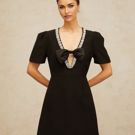 A short black mini dress with a bow embellishment worn by a model