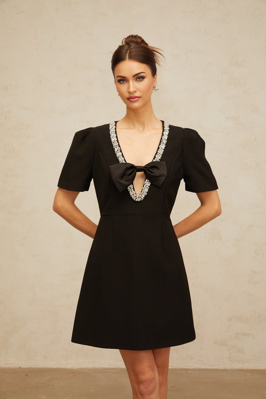 A short black mini dress with a bow embellishment worn by a model