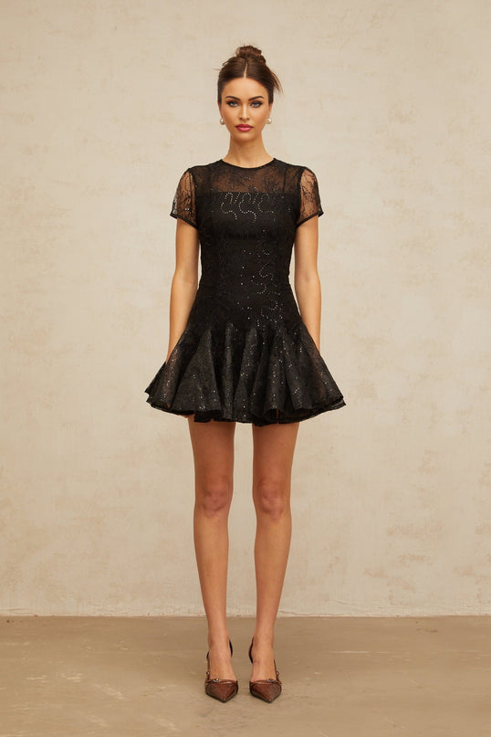 A short black mini dress with flared skirt covered in shimmering sequins worn by a model against a plain background