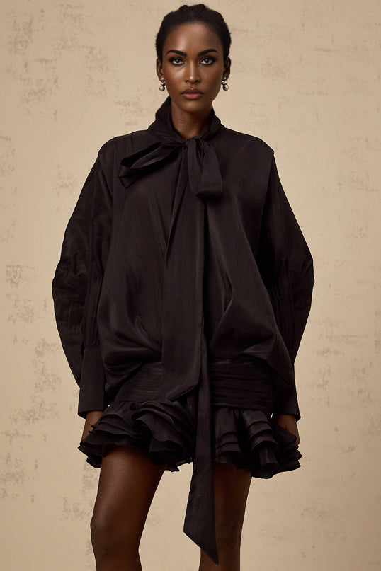 A short black mini dress with ruffled details and a pussybow neckline