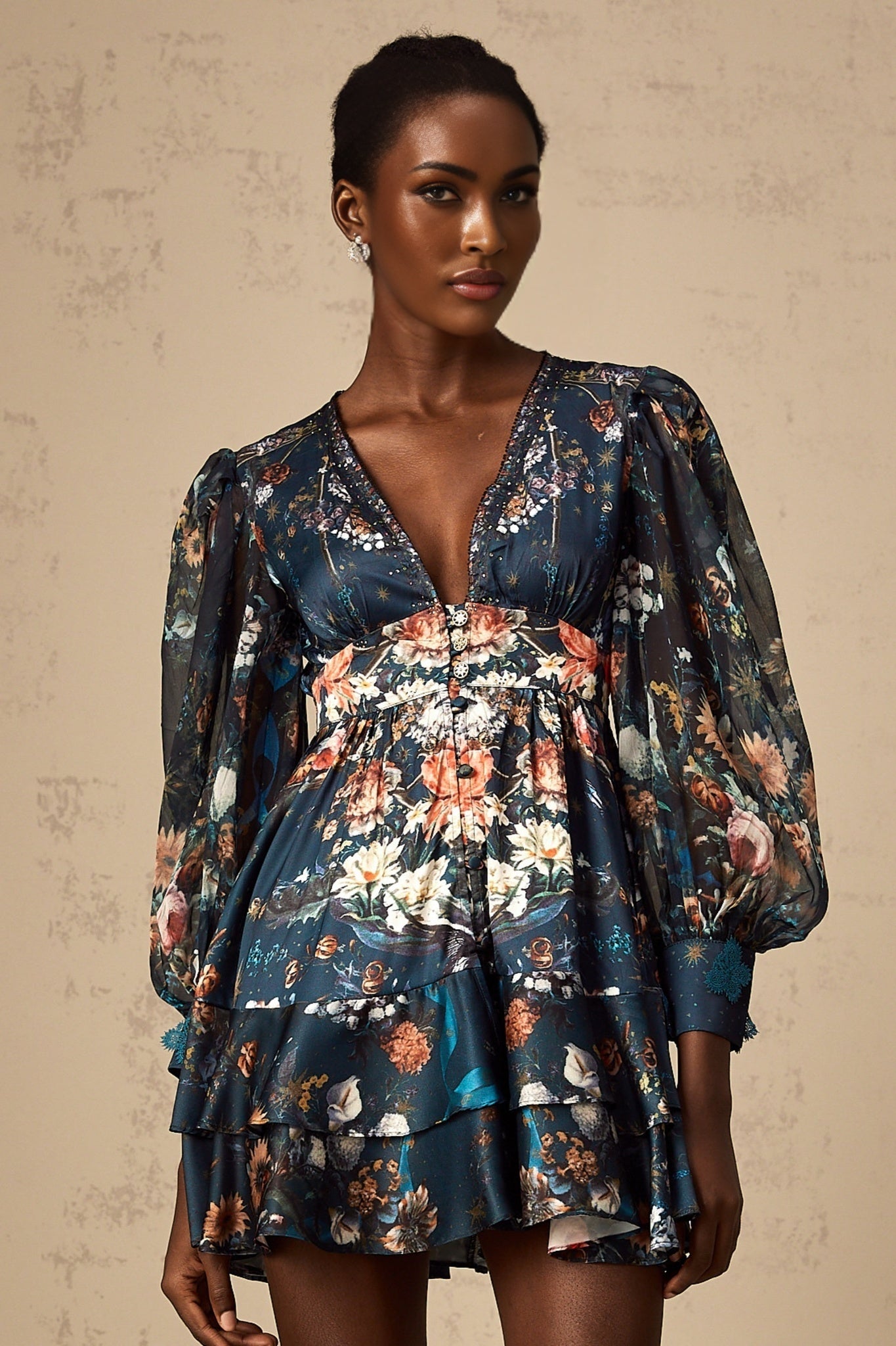A short blue mini dress with a graphic print pattern and embellishments worn by a model standing against a plain background