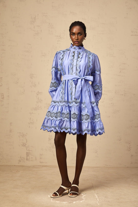 A short blue mini dress with tiered layers and intricate cutout embroidery details featuring a floral motif pattern throughout the fabric
