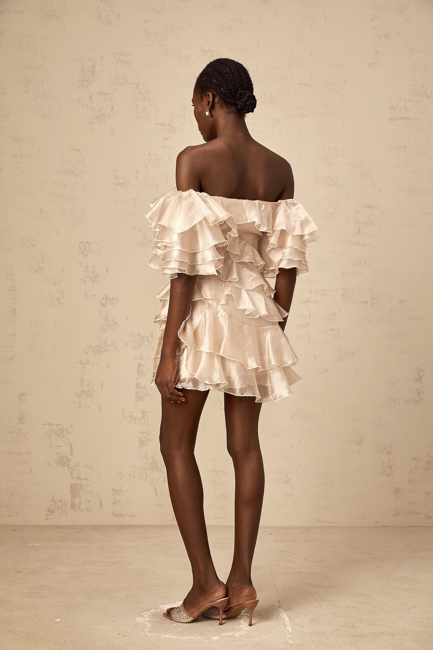A short flouncy dress in neutral tones with an asymmetric design featuring ruffles and a cerise pink accent color