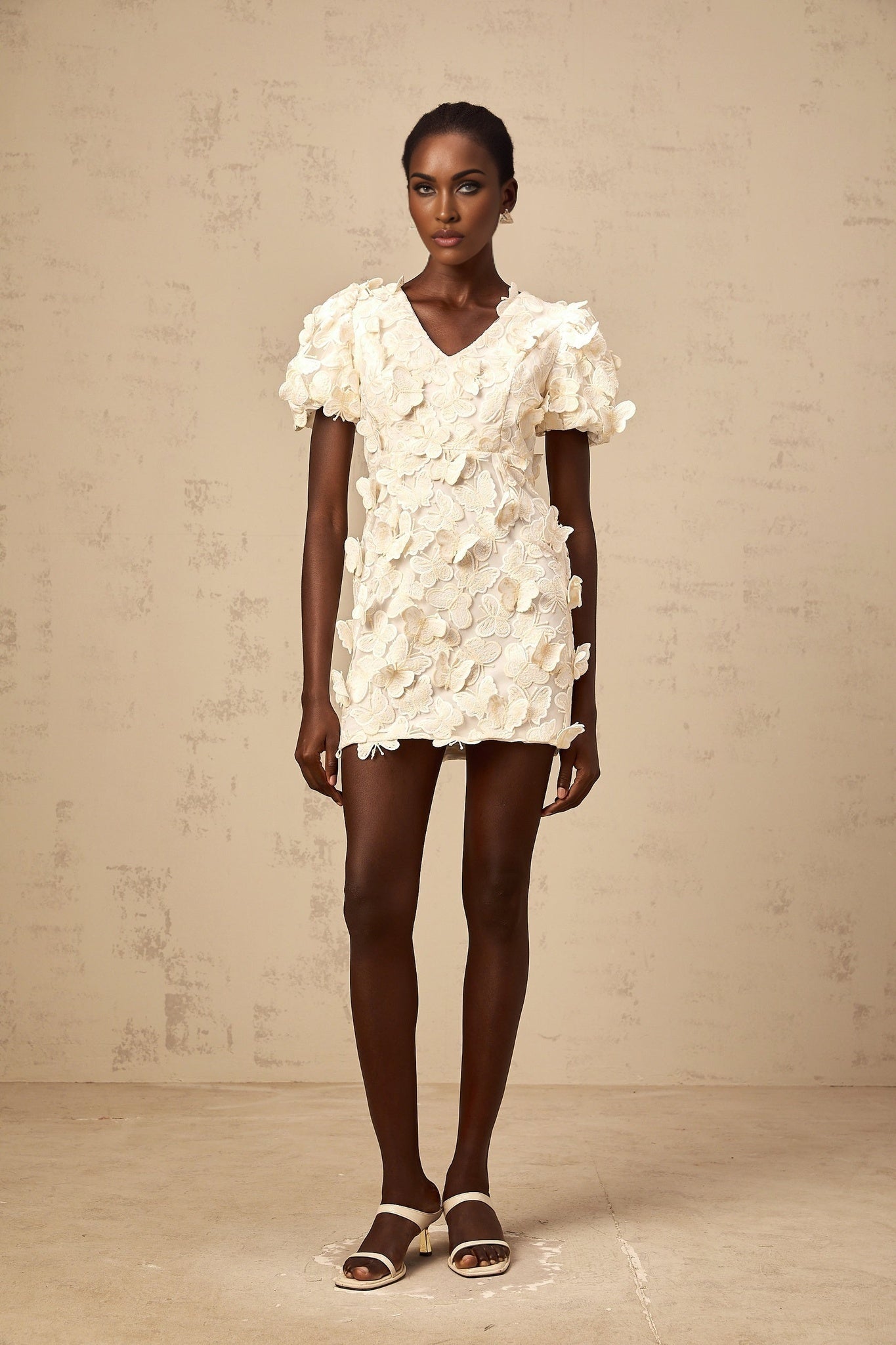 A short light colored dress with a flared Aline silhouette featuring decorative butterfly appliques and a mini length hemline