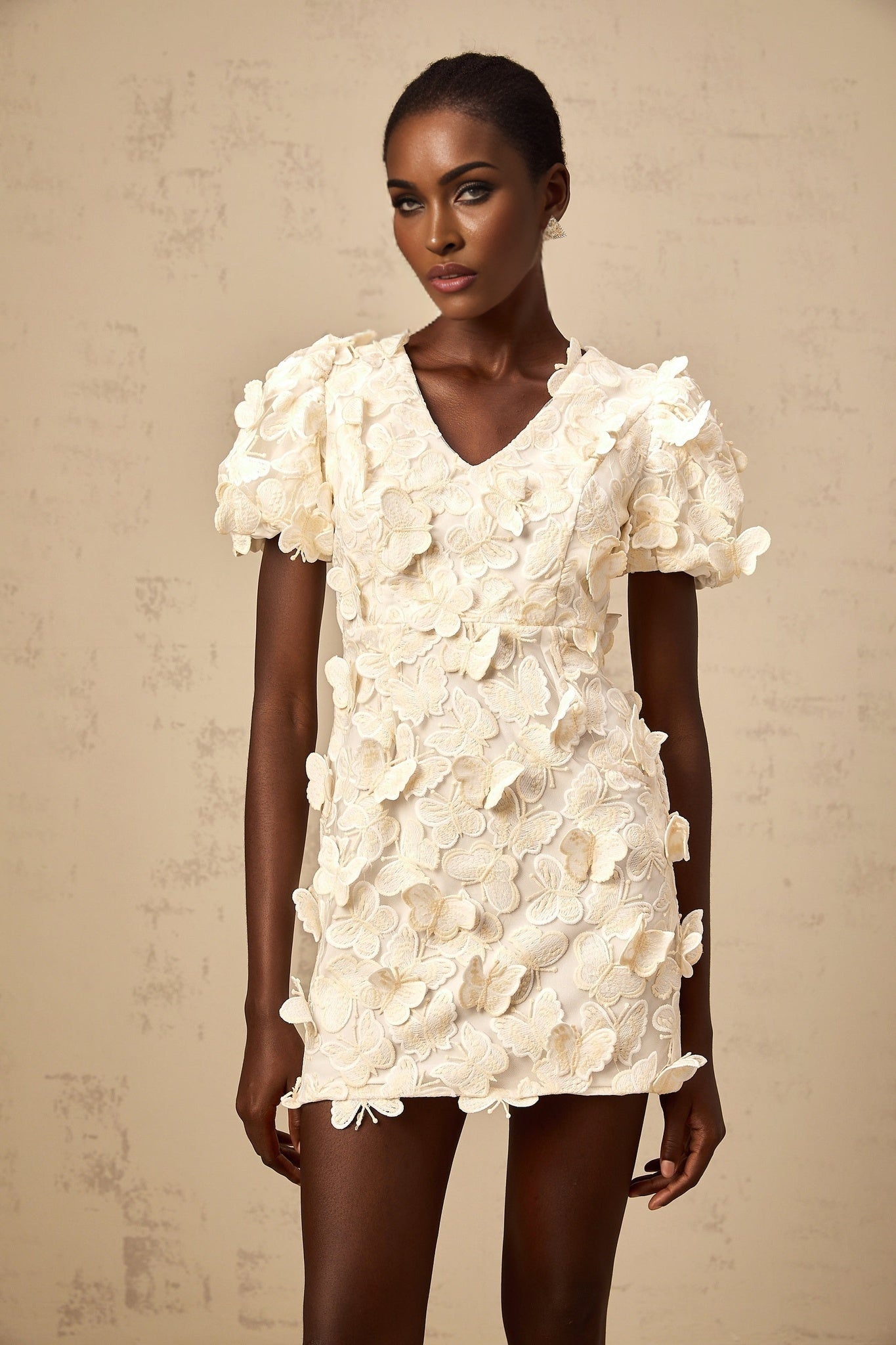 A short light colored dress with a flared Aline silhouette featuring decorative butterfly appliques and a mini length
