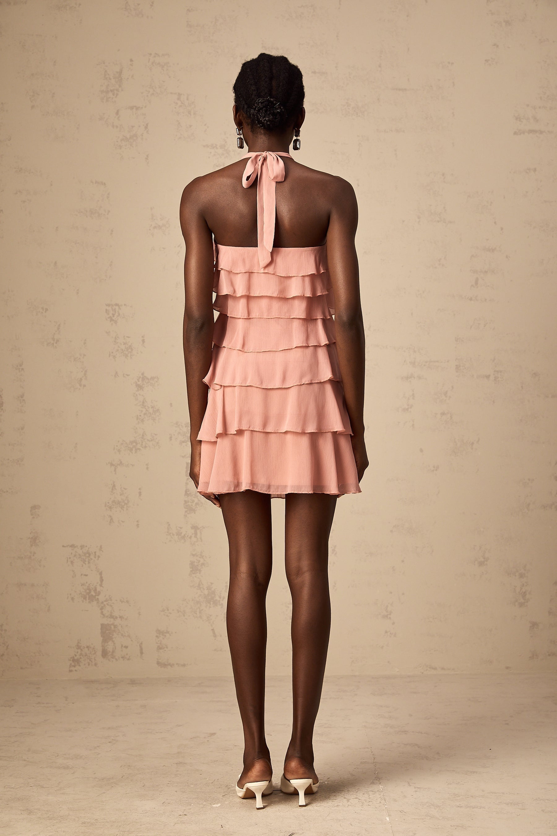 A short pink halter neck dress with multiple tiers creating a flowy silhouette The dress has a mini length and a vibrant briar pink color