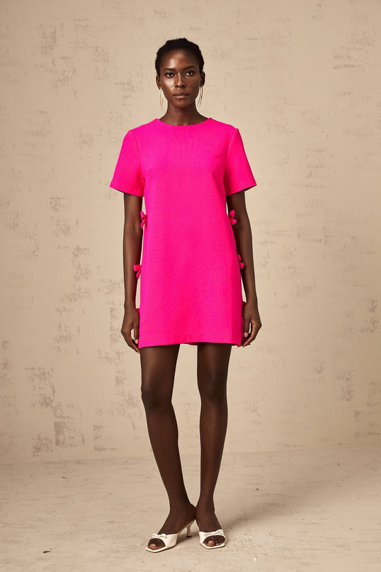 A short pink mini dress with a bow detail featuring a feminine and playful design