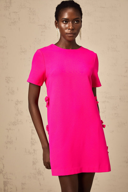 A short pink mini dress with a bow detail featuring a feminine and playful design