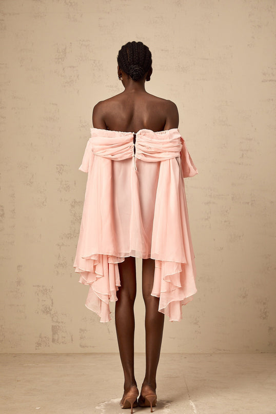 A short pink slip dress with a draped design and a bow detail worn by a model against a plain background
