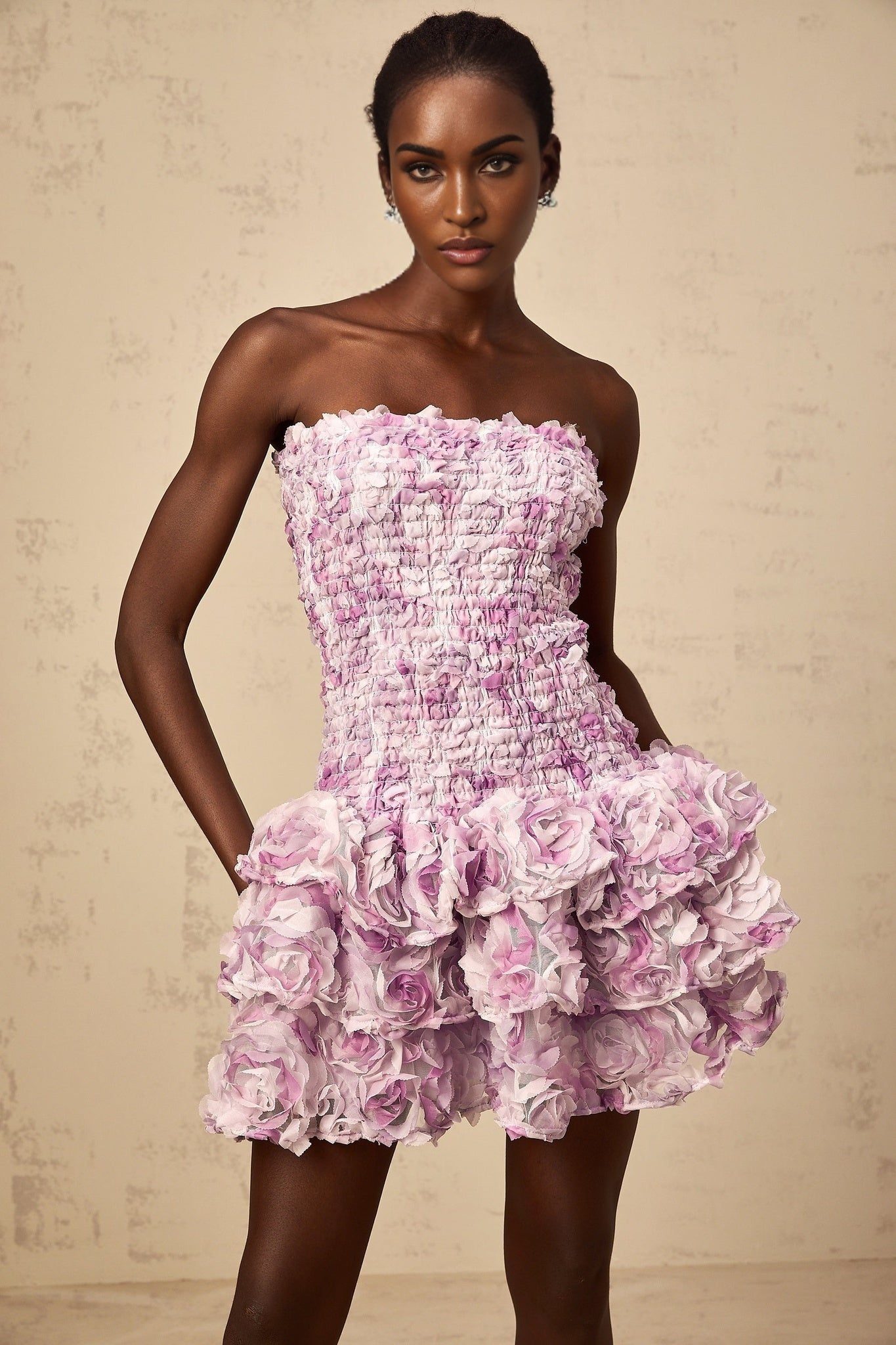 A short purple mini dress with tiered layers of tulle fabric featuring three dimensional petal details throughout creating a floral texture and voluminous silhouette