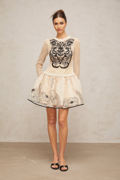 A short sleeveless mini dress with a floral jacquard pattern featuring contrasting color floral appliques for added texture and visual interest