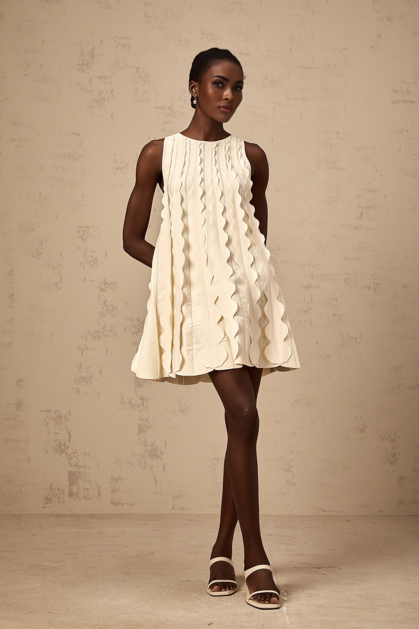 A short sleeveless white mini dress with wavy details along the edges named Axelle