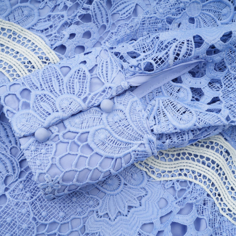 A short white dress with a Vneck and colorful floral embroidery details worn by a model standing against a plain background