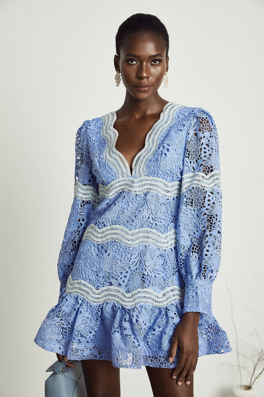 A short white mini dress with a Vneck and colorful floral embroidery details worn by a model against a plain background
