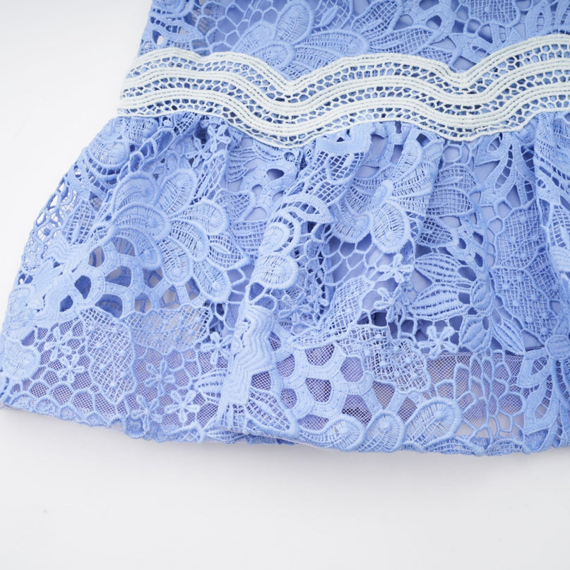 A short white mini dress with a Vneck and colorful floral embroidery details worn by a model standing against a plain background