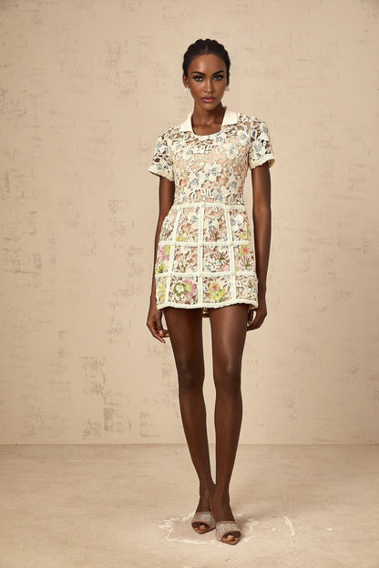 A short white mini dress with colorful floral embroidery patterns scattered across the fabric featuring a fitted waist and slightly puffed short sleeves