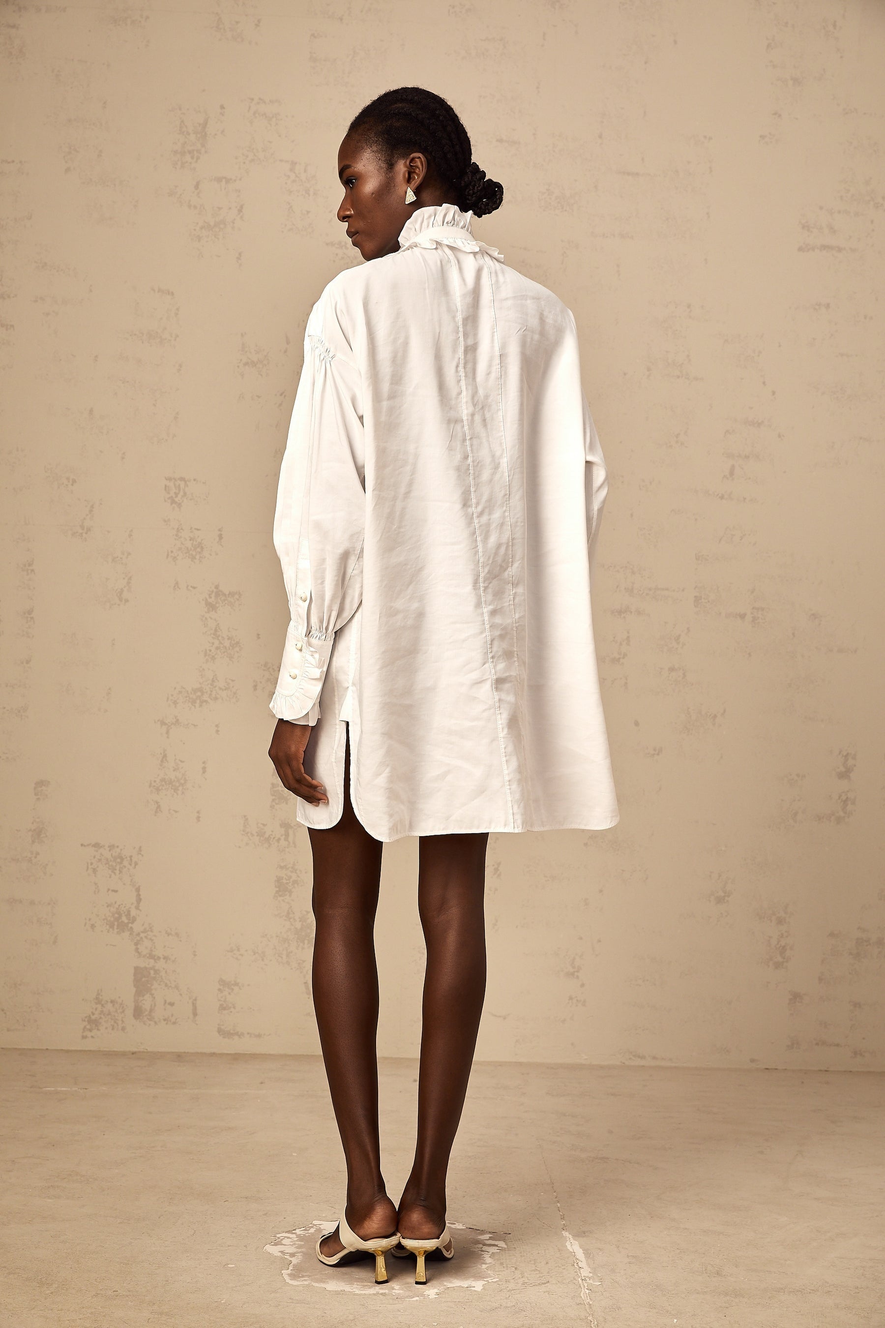 A short white mini dress with lace trim and ruffled details featuring a shirt style collar and buttonup front