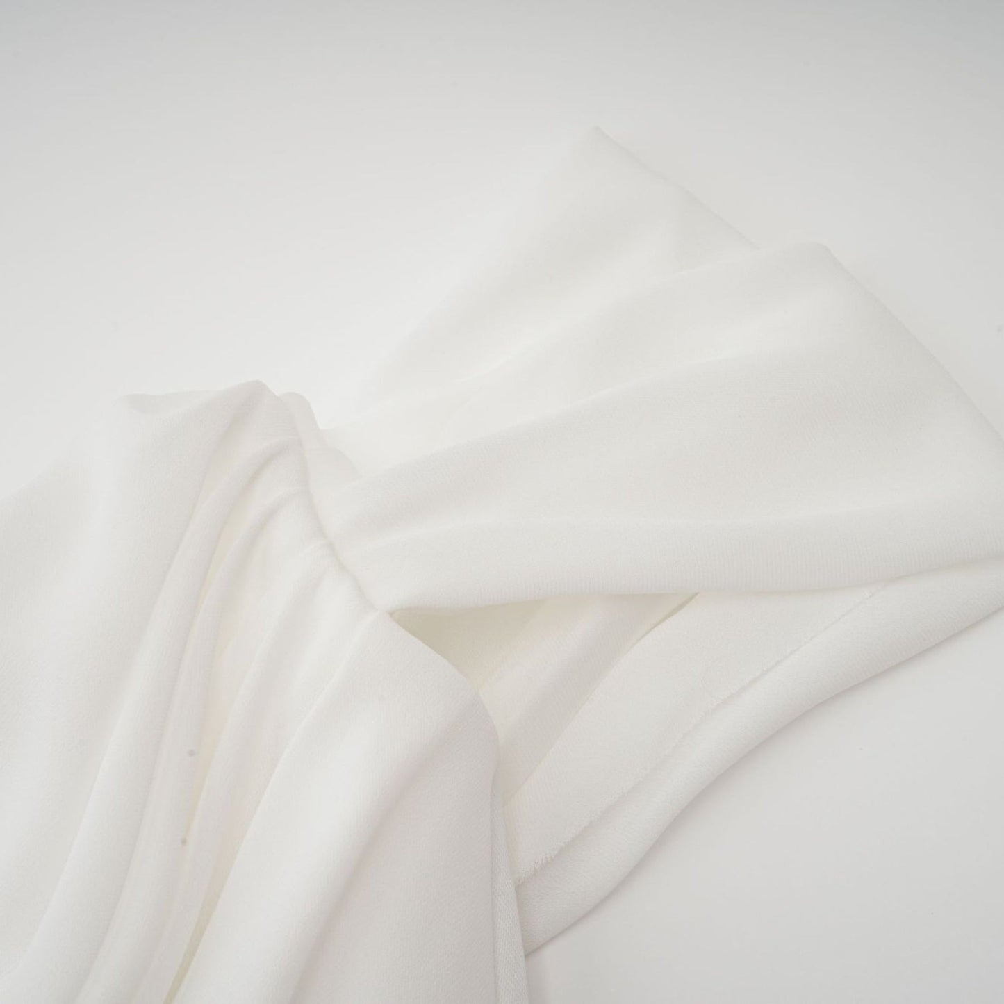 A short white mini dress with ruched fabric and ribbon details on a female model against a plain background