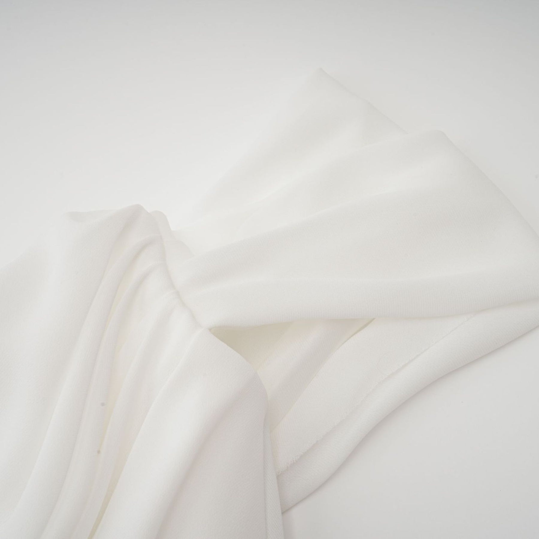 A short white mini dress with ruched fabric and ribbon details on a female model against a plain background