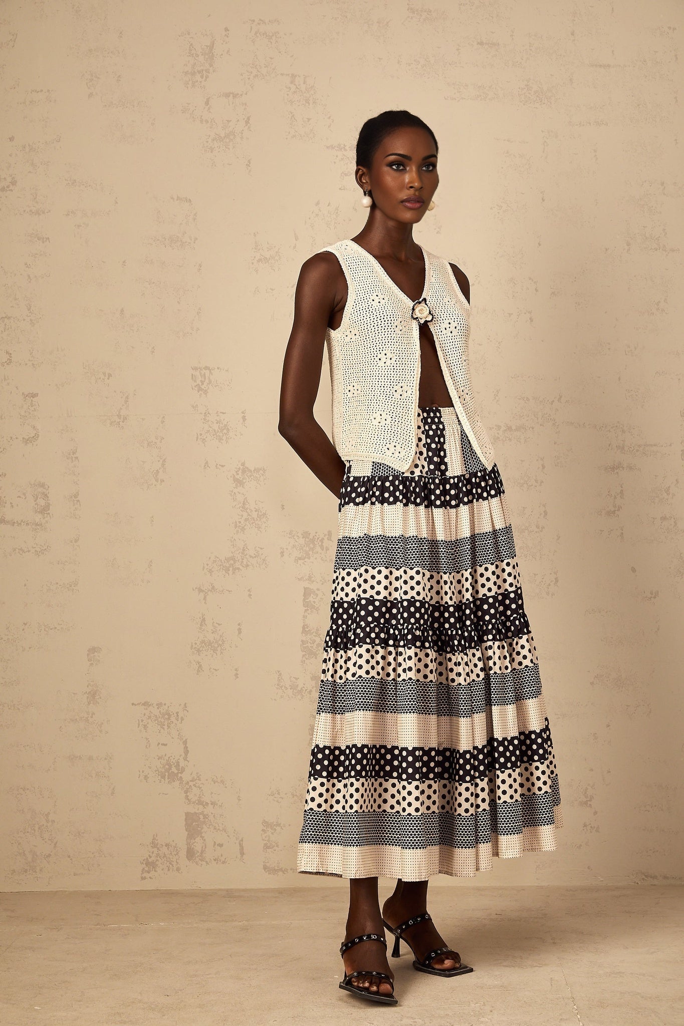 A sleeveless crochet knit tank top with an open front design in a light color featuring a delicate pattern and loose weave