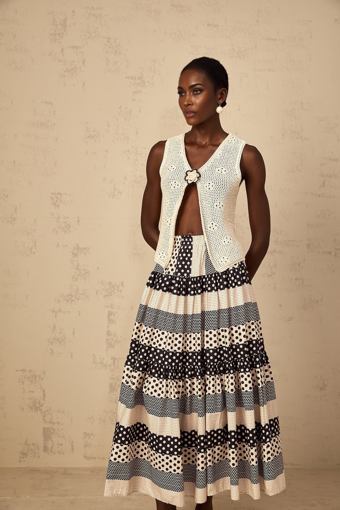 A sleeveless crochet knit tank top with an open front design in a light color featuring a loose and airy texture