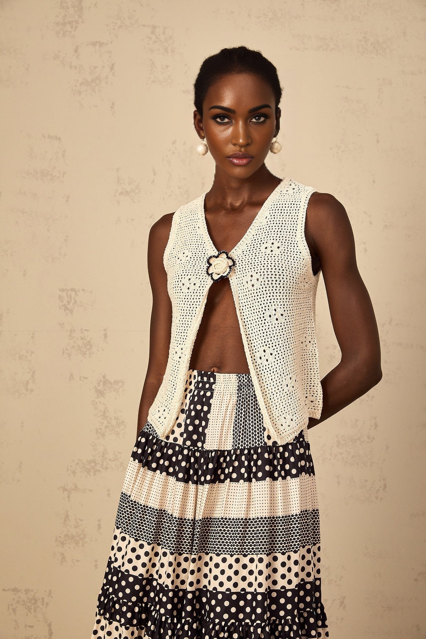 A sleeveless crochet knit tank top with an open front design in a light color hanging on display