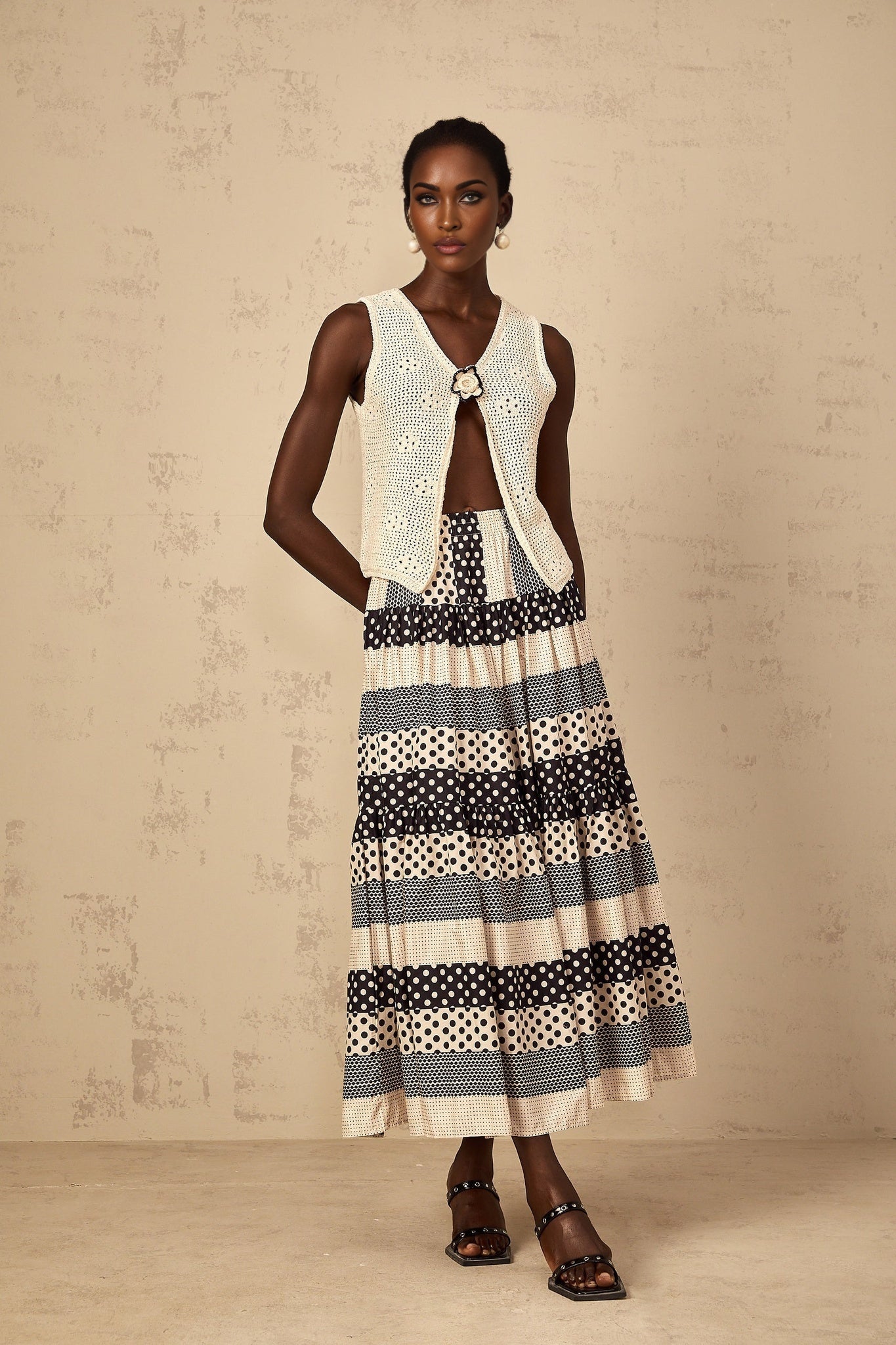 A sleeveless crochet knit tank top with an open front design in a light color worn by a model