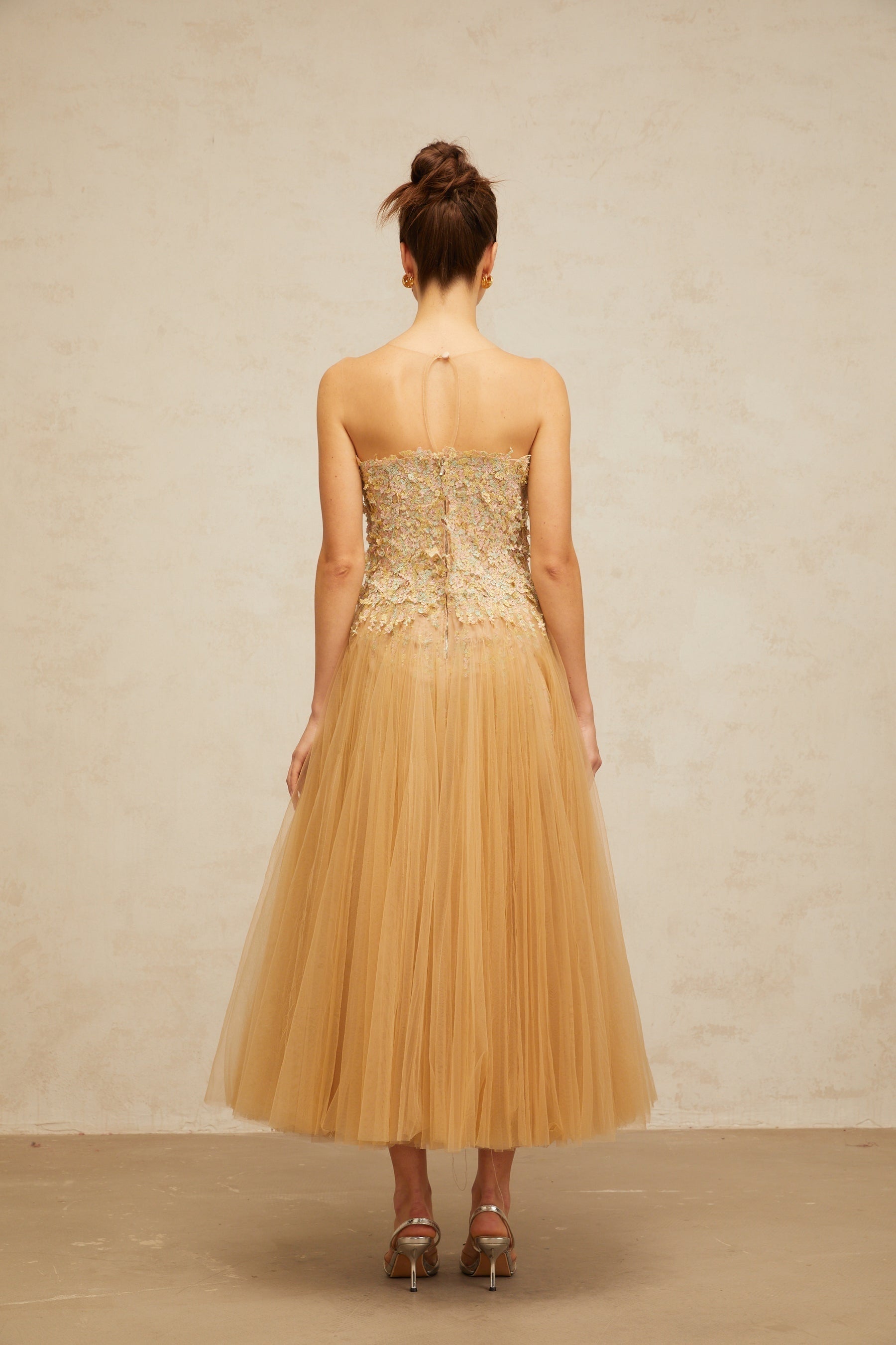 A sleeveless midi dress in neutral tones featuring pleated tulle fabric adorned with delicate sequins creating a shimmering effect throughout the garment