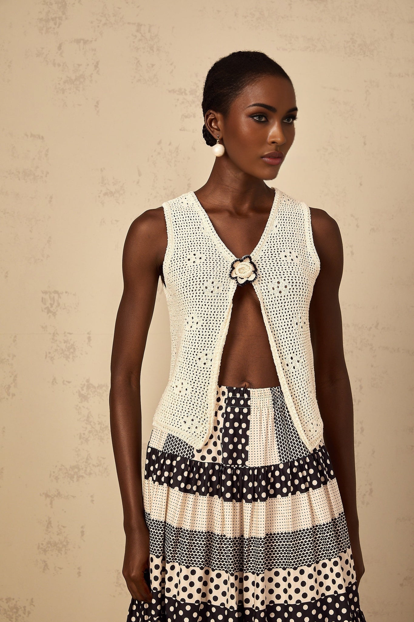 A sleeveless white crochet knit tank top with an open front design featuring a delicate floral pattern and scalloped edges