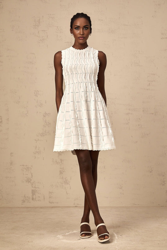 A sleeveless white knit mini dress with ruffled details worn by a model standing against a plain background