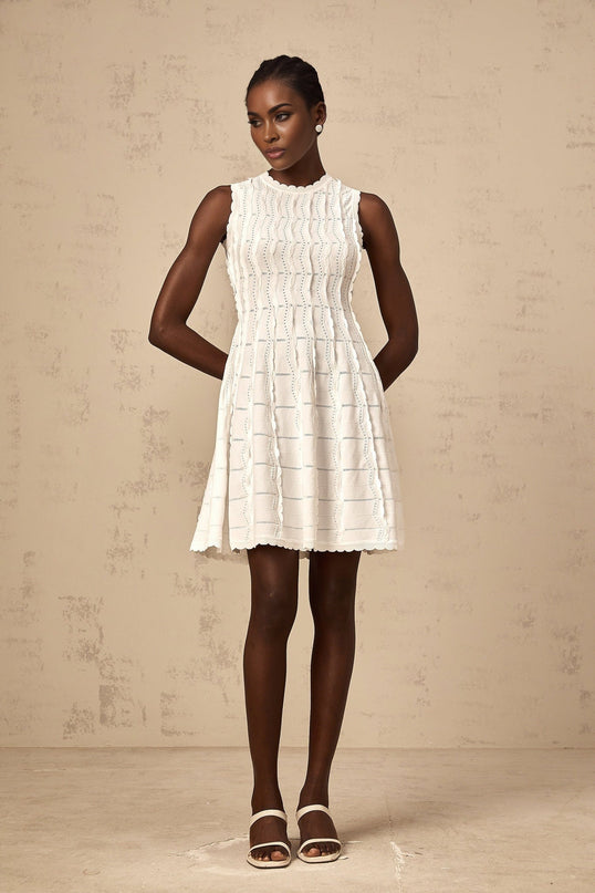 A sleeveless white knit mini dress with ruffled details worn by a model standing against a plain background