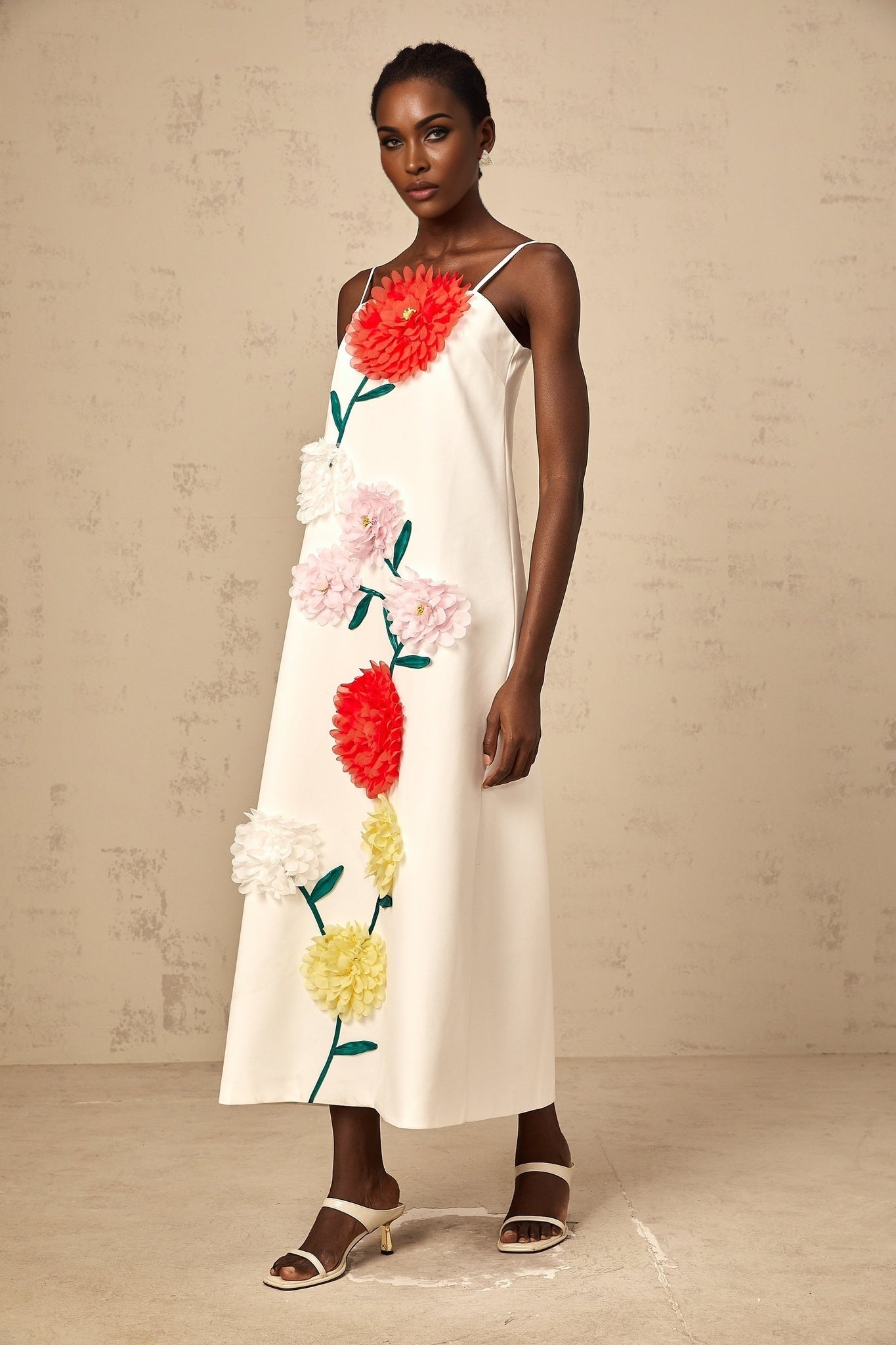 A sleeveless white midi dress with 3D floral petal details covering the bodice and skirt creating a textured appearance