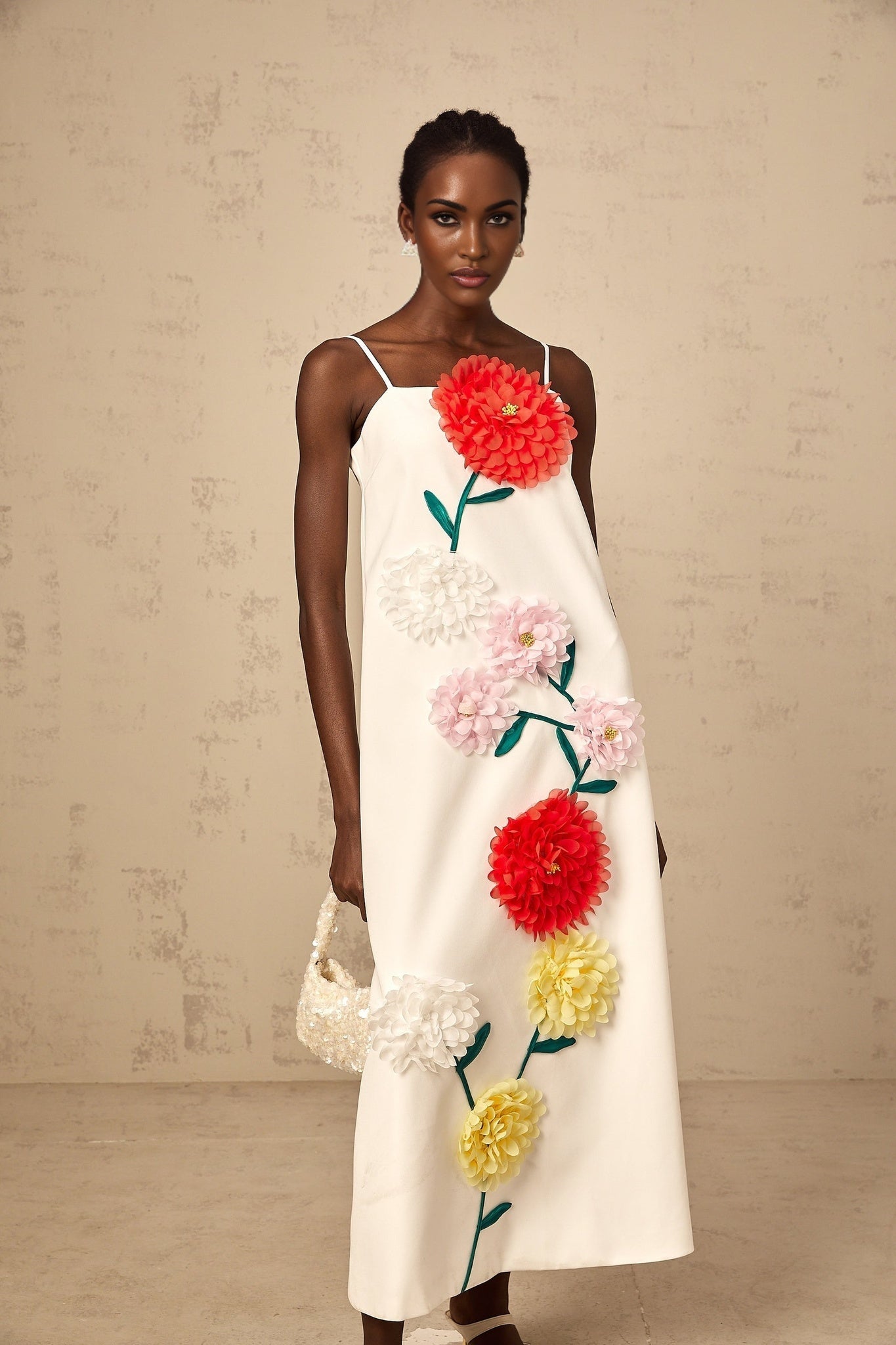 A sleeveless white midi dress with three dimensional floral petal details covering the bodice