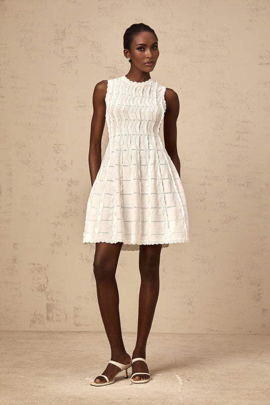 A sleeveless white mini dress with a knit texture and ruffled details worn by a model