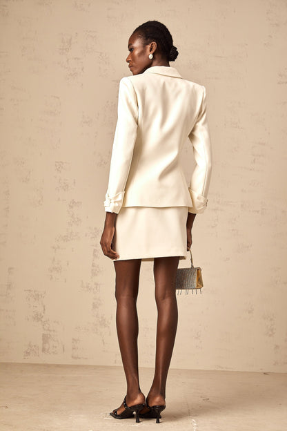 A white blazer and skirt set featuring a cinched waist on the blazer and crystal embellishments both pieces matching in style and color