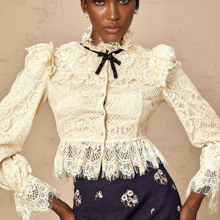 A white blouse with a bow detail at the neckline and delicate floral lace pattern throughout the garment