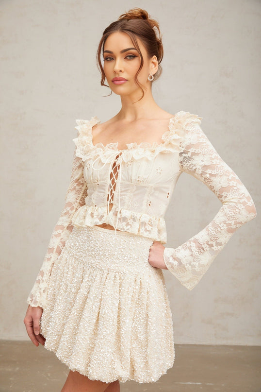 A white blouse with floral lace pattern and ruffled details shown on a plain background