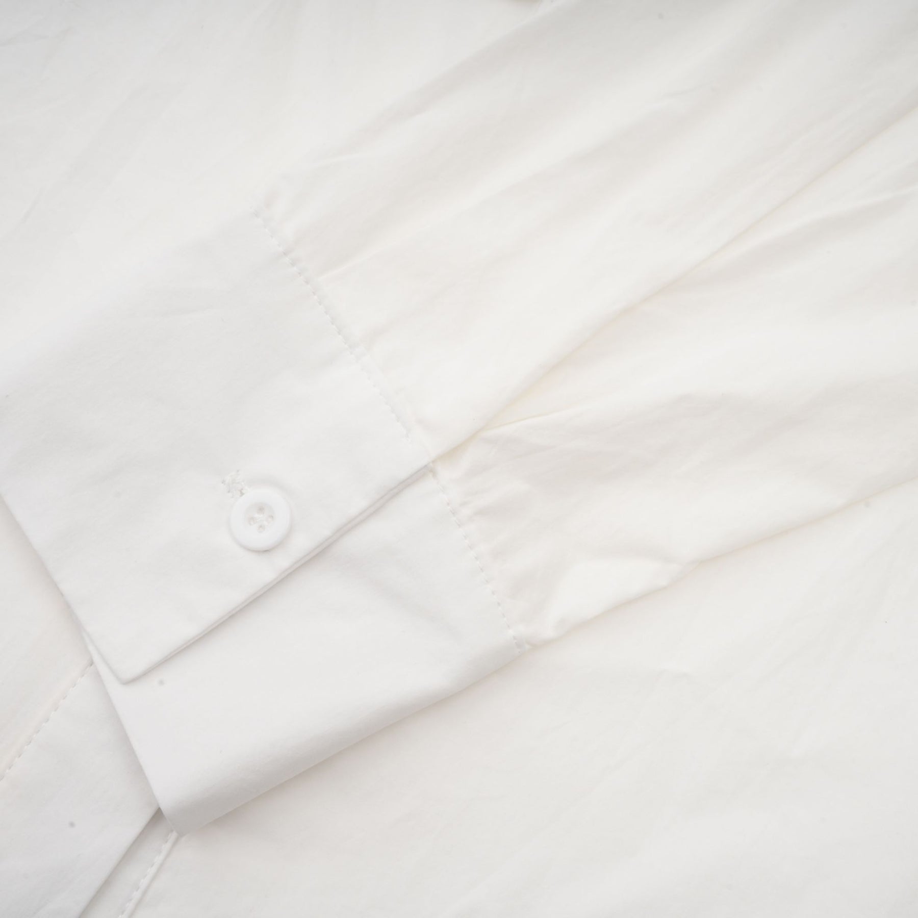 A white buttonup shirt with floral cutout patterns visible on the sleeves and body featuring a relaxed fit and collar