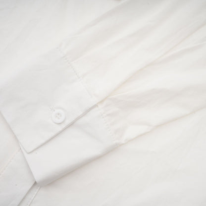 A white buttonup shirt with floral cutout patterns visible on the sleeves and body featuring a relaxed fit and collar