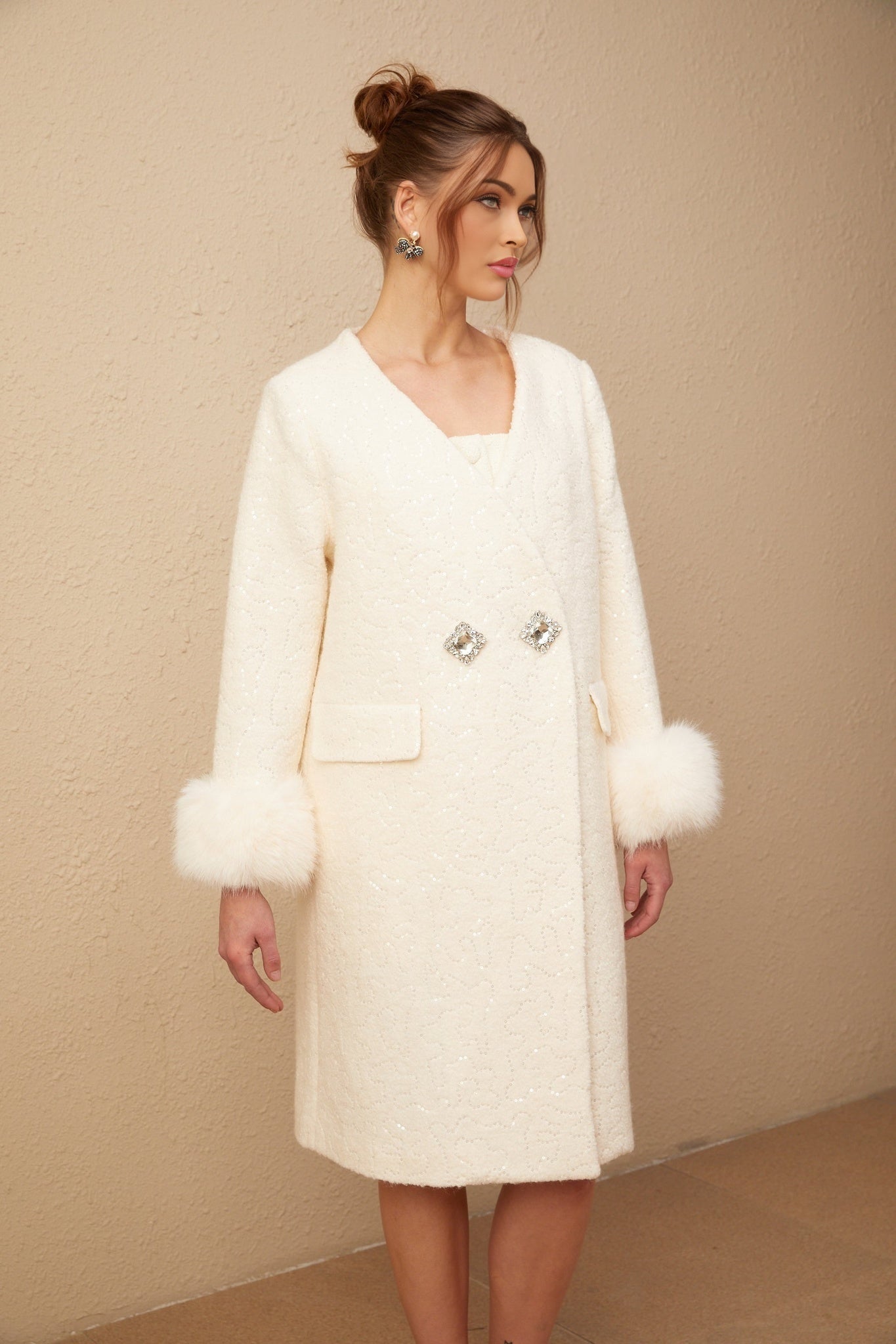 A white collarless coat made of textured fur fabric worn by a model against a plain background