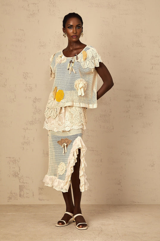 A white crochet knit top with delicate lace panels featuring an intricate floral pattern and scalloped edges