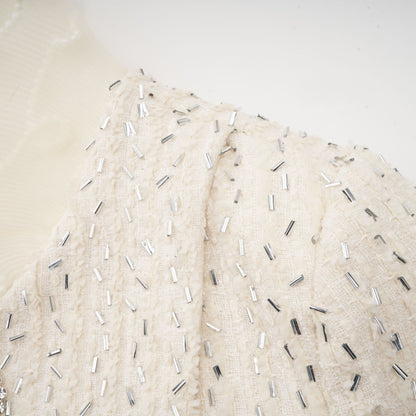 A white cropped jacket with beaded details and ruffle trim featuring short sleeves and an open front design
