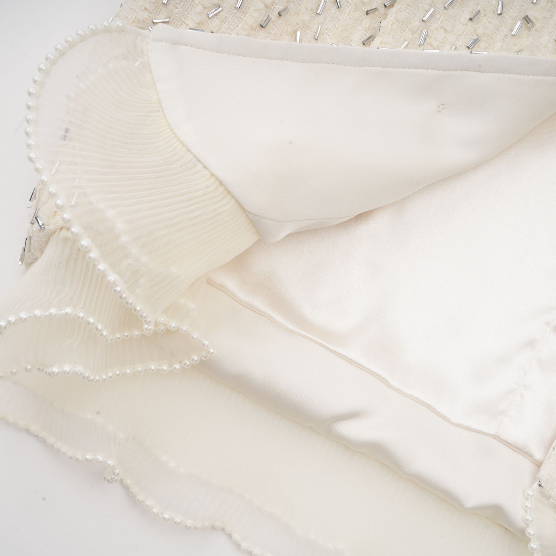 A white cropped jacket with beaded embellishments and ruffle details along the edges