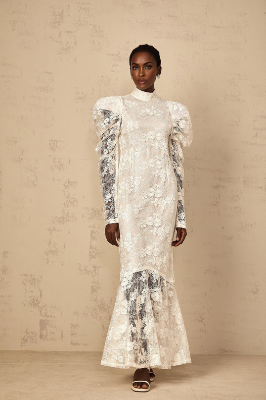 A white floorlength mermaid style dress with floral lace detailing covering the entire garment featuring a fitted bodice and flared skirt